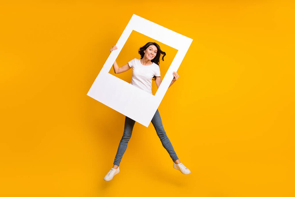 Full length body size view of lovely cheerful girl jumping having fun holding photo frame isolated over bright yellow color background - Fotografie, Obrázek