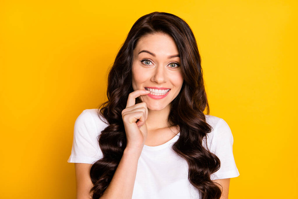 Photo of adorable tricky young lady dressed white t-shirt smiling biting finger isolated yellow color background - Photo, image