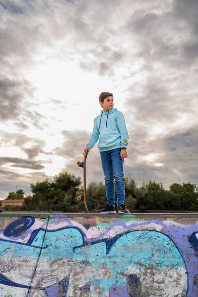 Χαριτωμένος έφηβος σε ένα πάρκο skate ενάντια σε ένα συννεφιασμένο ουρανό - Φωτογραφία, εικόνα