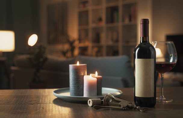 素晴らしい赤ワインの試飲:ボトル、ワイングラス、リビングルームのテーブルの上にライトキャンドルやコルク栓ネジ - 写真・画像