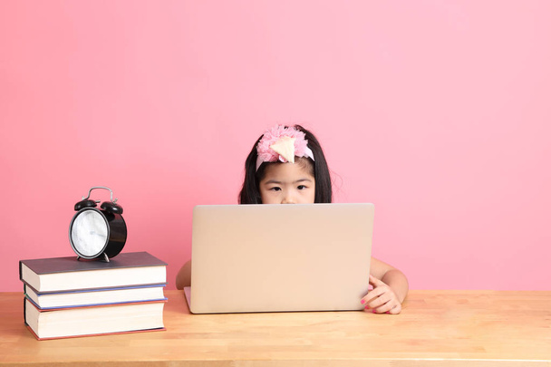 Милая азиатка учится через интернет на ноутбуке с розовым фоном. - Фото, изображение