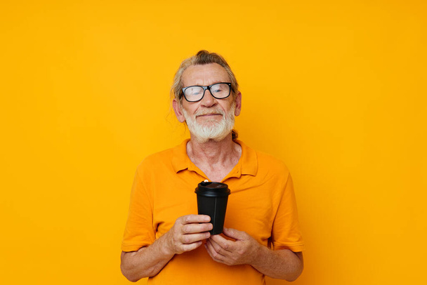 Photo of retired old man in a yellow T-shirt a glass with a drink isolated background - Foto, Imagen