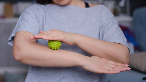 Крупним планом молода жінка відпрацьовує м'язи рук зеленим міофасциальним м'ячем. Жінка виконує вправи з гумовим м'ячем
 - Фото, зображення