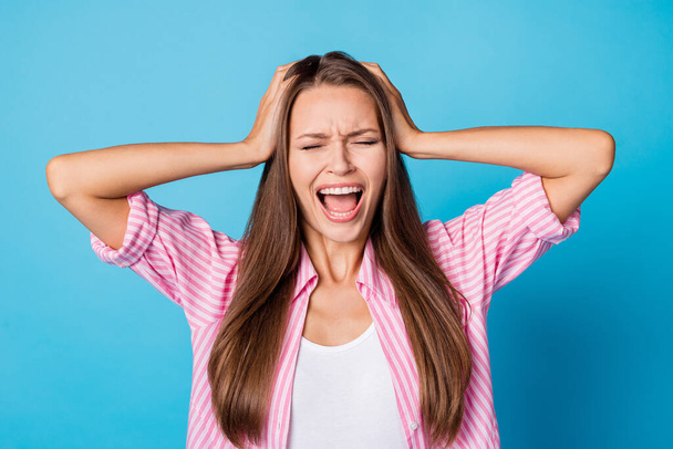 Photo of angry overwhelmed crazy young lady hands hold head open mouth wear pink striped shirt isolated blue background - 写真・画像