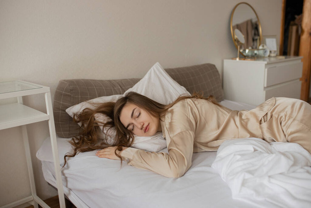 A young girl in stylish pajamas sleeps on a white bed. - Zdjęcie, obraz
