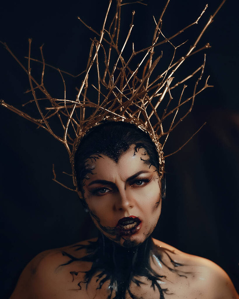 Fantasy portrait of emotional gothic woman dark witch. Girl goddess in in golden crown from branches. Beautiful face black art makeup. Art photo, black background - Foto, Imagen