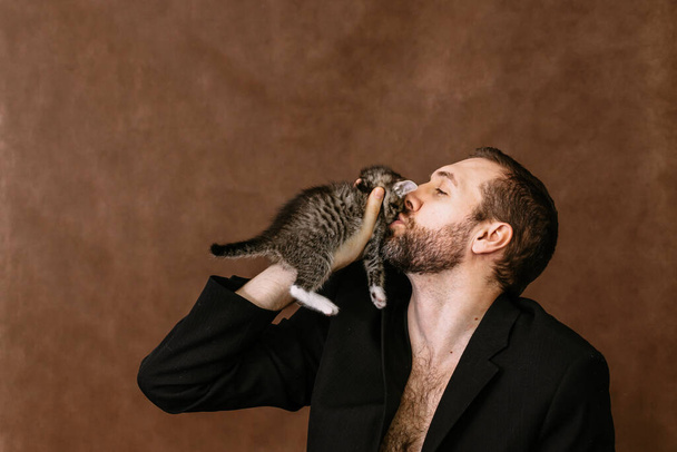 man plays with a kitten. Hugs him and kisses him - Photo, image