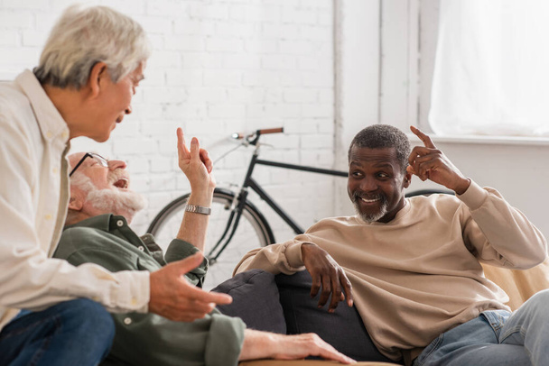 Veselí multikulturní starší muži mluví doma na gauči  - Fotografie, Obrázek