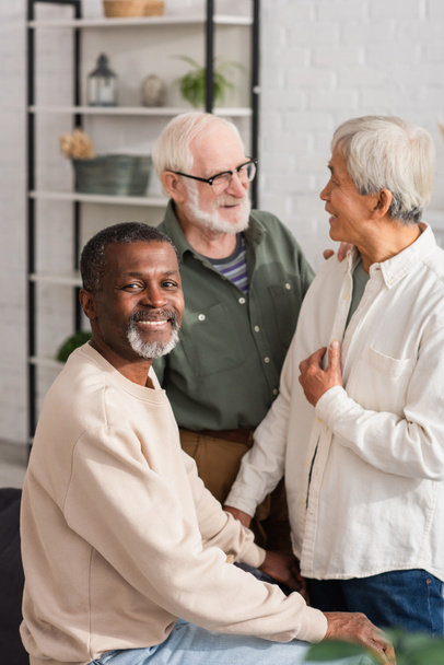 Afro-Amerikaanse man lacht op camera in de buurt van multi-etnische gepensioneerden thuis  - Foto, afbeelding