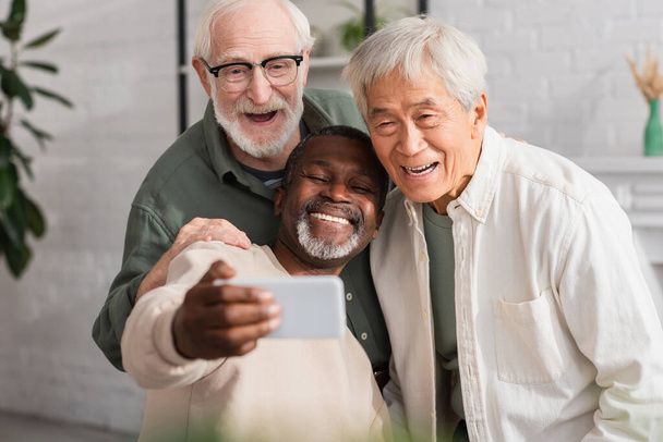 Lächelnde multikulturelle Freunde, die zu Hause ein Selfie auf dem Smartphone machen  - Foto, Bild