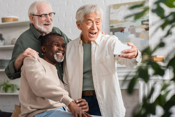 Senior asian man taking selfie near multiethnic friends at home  - 写真・画像