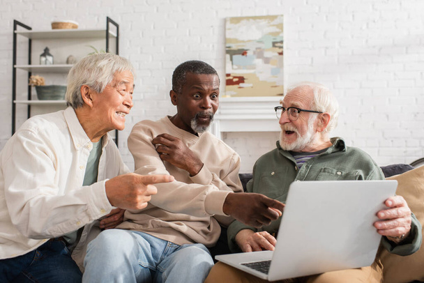 Excited african american man pointing at laptop near multiethnic friends at home  - Φωτογραφία, εικόνα