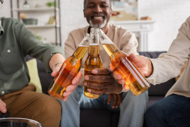 Blurred interracial friends clinking beer at home  - Foto, Bild