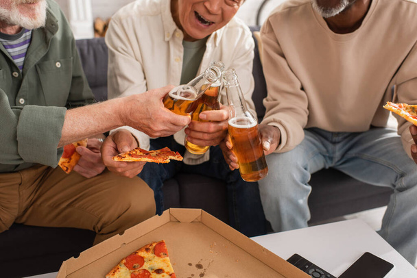 Ausgeschnittene Ansicht von interrassischen Rentnern, die mit Bier klingeln und zuhause Pizza halten  - Foto, Bild