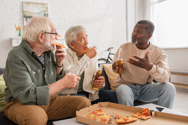 Africano americano com cerveja conversando com amigos inter-raciais sênior comer pizza em casa  - Foto, Imagem