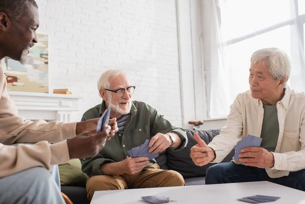 Ancianos hombres multiétnicos jugando a las cartas en la sala de estar  - Foto, imagen