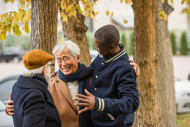 Mutlu Asyalı adam, şehir sokağında ırklar arası arkadaşlara sarılıyor.  - Fotoğraf, Görsel