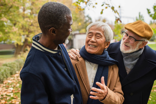 Allegro uomo asiatico che parla con amici multietnici nel parco autunnale  - Foto, immagini