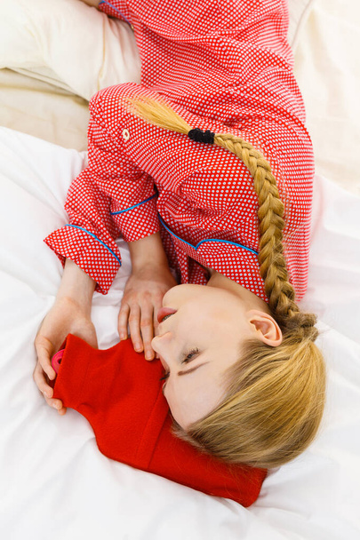 Woman lying on bed sleeping with warm red hot water bottle. Fever, flu treatment objects concept. - Foto, Bild