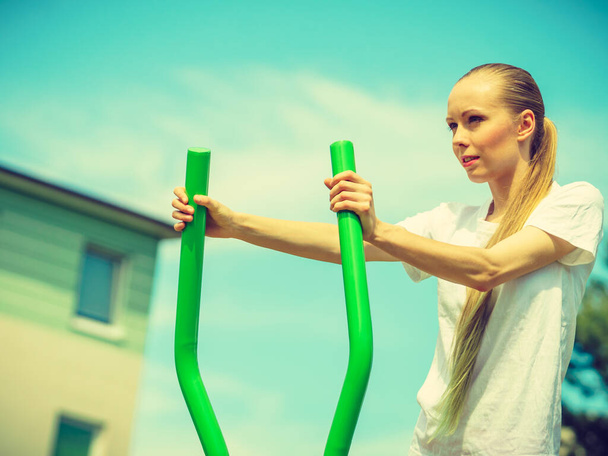 Woman making exercises on public equipment in city park. Girl working out in outdoor gym. Healthy lifestyle. - 写真・画像