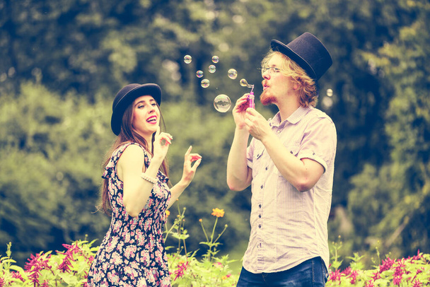 Happy funny hipster couple playing together blowing soap bubbles outdoor in spring park. - Valokuva, kuva