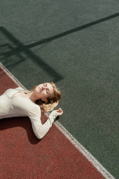 Jovem loira mulher deitada em um campo de esporte backetball wih seus olhos fechados - Foto, Imagem