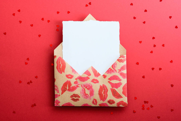 Valentine letter concept. Envelope with blank white note mockup inside and Valentines hearts confetti on red background. - Zdjęcie, obraz