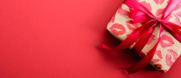 Valentines Day gift box wrapped craft paper with lipstick marks print with red ribbon bow on red background. Valentines day present, surprise. Top view with copy space. - Zdjęcie, obraz