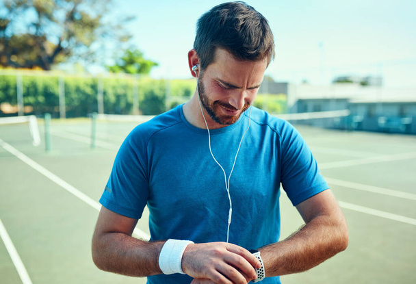 Ik ben goed met de tijd. Opname van een sportieve jongeman die zijn horloge checkt tijdens het sporten op een tennisbaan. - Foto, afbeelding