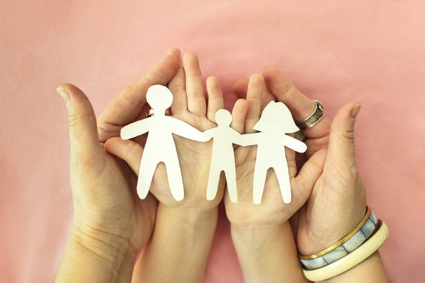 Cropped shot of mother, father and child holding family paper cut out in hands, isolated on pink background. cardboard figures of parents and kid holding hands together. International Day of Families - Photo, Image