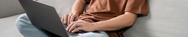 Technology Concept Ο άνδρας που φοράει καθημερινά ρούχα κάθεται στον καναπέ, ξεκουράζει το σημειωματάριό του στην αγκαλιά του και κάνει τη δουλειά του. - Φωτογραφία, εικόνα