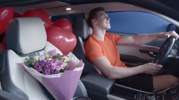 Een gelukkige man rijdt in een auto met een boeket bloemen. Cadeaus - Video