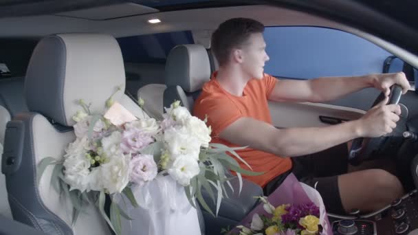 Szczęśliwy facet jeździ samochodem z bukietem kwiatów. Prezenty - Materiał filmowy, wideo