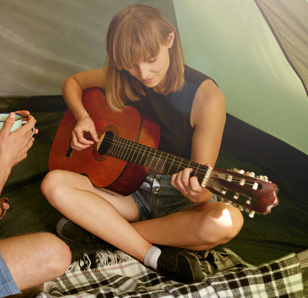 Teen leirimusiikkia. Ammuttu nuori nainen soittaa kitaraa poikaystävänsä teltassa. - Valokuva, kuva