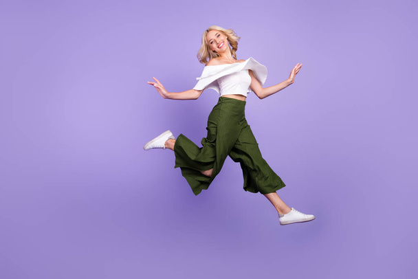 Photo of carefree lady jump go run wear white blouse flared trousers isolated violet color background - Foto, Imagen