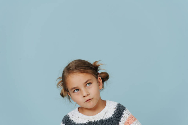 Looking up tight-lipped little girl in striped sweater, hair in buns over blue. A lot of copy space around. - Foto, immagini
