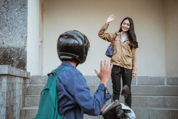 Asian woman waving to someone picking her on a motorbike - 写真・画像