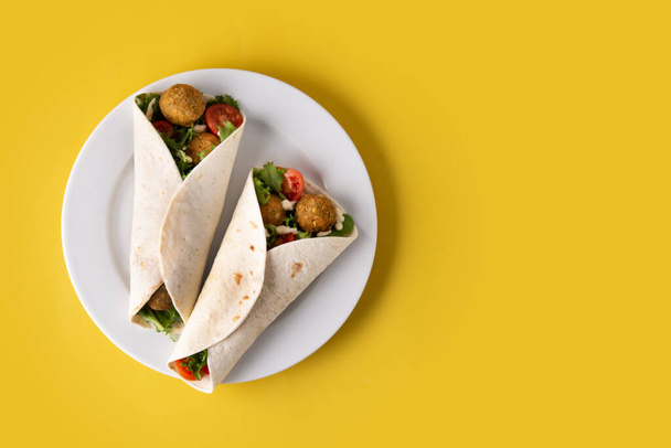 Tortilla wrap with falafel and vegetables on yellow background - Zdjęcie, obraz