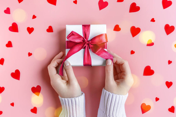 Női kéz kezében egy ajándék fehér csomagolópapír rózsaszín háttér piros szív - Fotó, kép