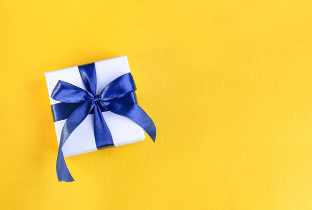 Banner of a Gift wrapped in white paper with a blue bow made of satin on festive yellow orange background - Photo, Image