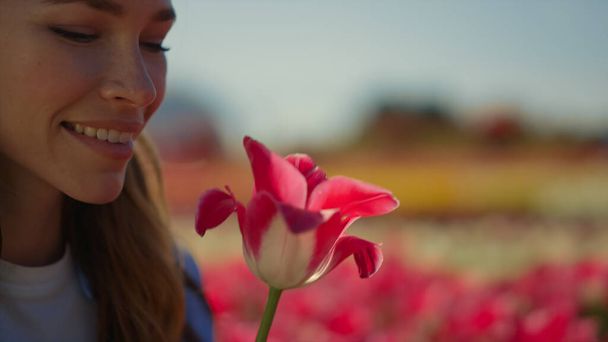 Closeup woman face looking at fresh spring flower. Happy woman holding red tulip - Foto, immagini