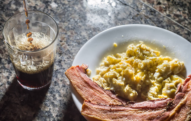tranches de bacon sur une assiette avec des œufs brouillés et une tasse de café sur le côté - Photo, image