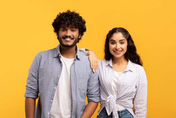 Millennials felici. Ritratto di coniugi indiani romantici che posano su sfondo giallo e sorridono alla macchina fotografica - Foto, immagini