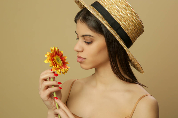 Studio shot of beautiful young woman in straw hat holds Transvaal daisy flower. - Foto, afbeelding