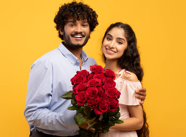 Πορτρέτο της αγάπης ζευγάρι ινδική με δέσμη των λουλουδιών χαμογελώντας και κοιτάζοντας κάμερα, γιορτάζει την Ημέρα του Αγίου Βαλεντίνου - Φωτογραφία, εικόνα