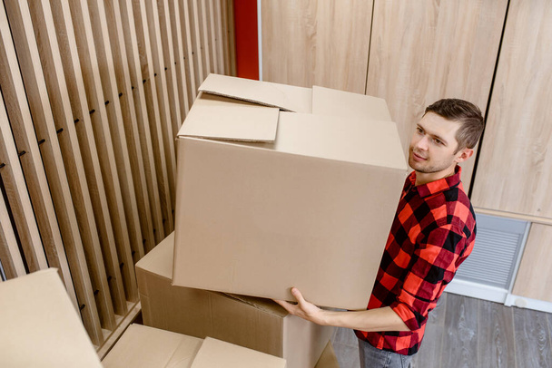 Young man, a courier, is carrying a cardboard box in a post office store. Delivery parcel concept - Foto, Bild