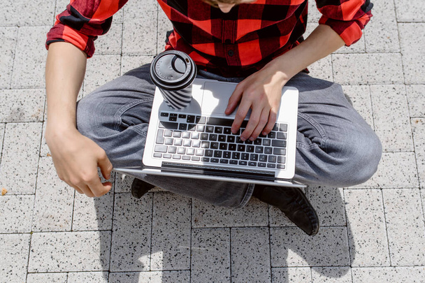 Вид сверху: человек-фрилансер работает на улице на ноутбуке и пьет кофе. Работа везде концепция - Фото, изображение