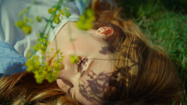 Relajada mujer redhar tocando la cara con flor de primavera sobre fondo de hierba verde. - Foto, imagen