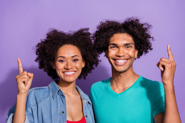 Pozitif, neşeli, genç Afro-Amerikan çiftin fotoğrafı mor arka planda izole edilmiş boş bir yeri işaret ediyor. - Fotoğraf, Görsel