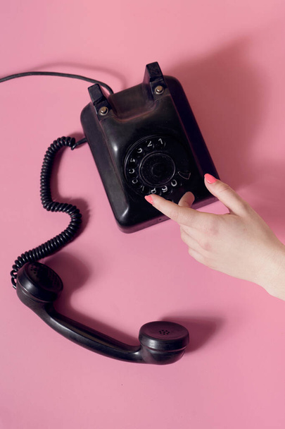 Kreatív retro stílusú vizuális női kéz és vintage telefon. Folyamatos híváskoncepció. Lapos laikus kompozíció pasztell rózsaszín háttér. - Fotó, kép